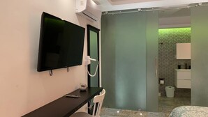 A hotel room with a TV, desk, chair, and a shower area with a green-lit wall. - Luxury Apartments Bello (Punta Cana)