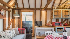 A cozy room with a wooden ceiling, a sofa with patterned pillows, a television, a dining table with a checkered tablecloth, and a kitchen area with a microwave and a bottle of wine. - The Granary by Bloom Stays - cute lodge sleeps 2 guests  in 1 bedroom (Canterbury)