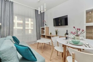 A modern living room with a sofa, dining table, chairs, a TV, and a window with curtains.