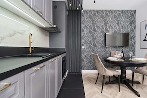 Une cuisine moderne avec un plan de travail noir, un robinet doré et un coin repas comprenant une table ronde et des chaises.