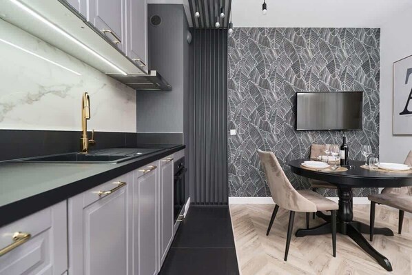 Une cuisine moderne avec un plan de travail noir, un robinet doré et un coin repas comprenant une table ronde et des chaises.