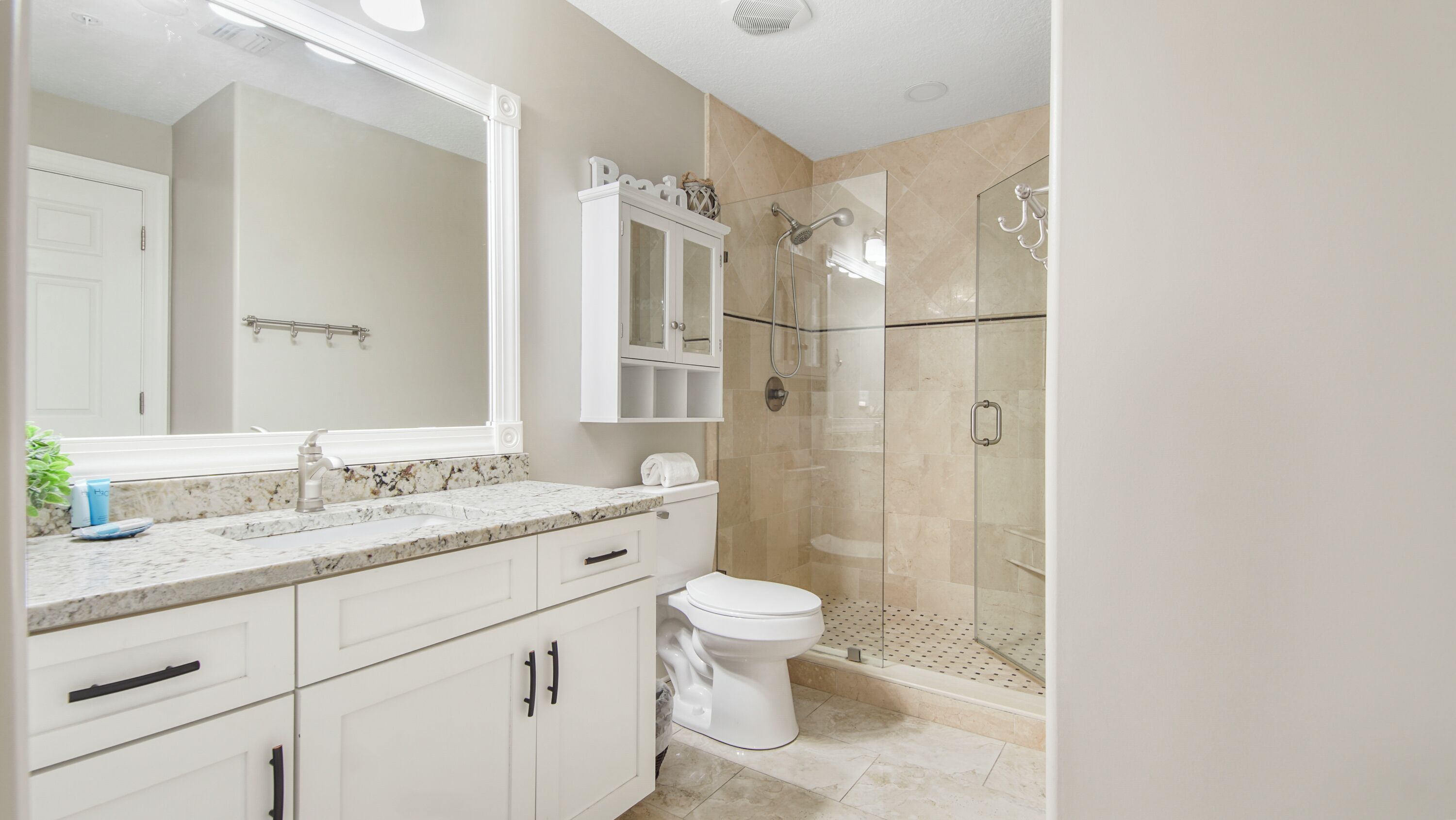 A modern bathroom with a marble countertop, a large mirror, a toilet, a shower with glass doors, and a cabinet above the sink.
