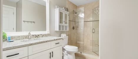 A modern bathroom with a marble countertop, a large mirror, a toilet, a shower with glass doors, and a cabinet above the sink.