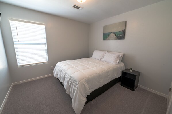 A bedroom with a bed, a nightstand, a window, and a painting on the wall.