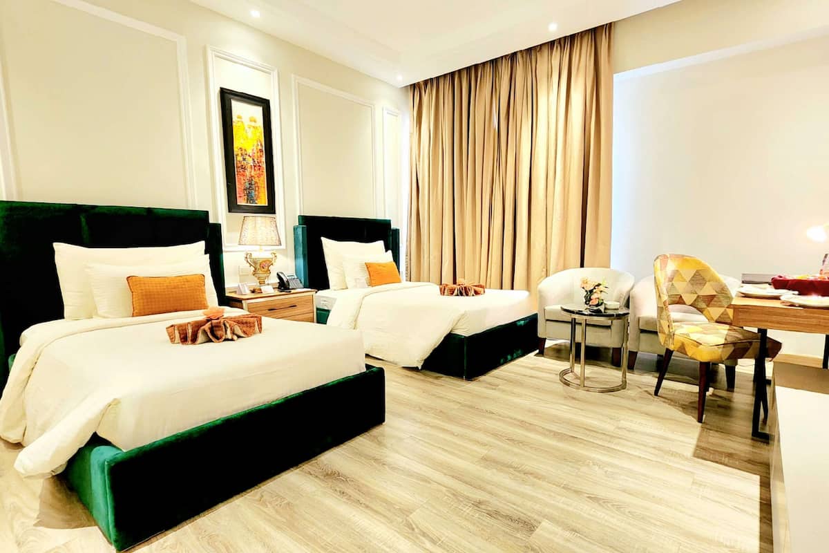Habitación de hotel con dos camas, un escritorio, una silla, un televisor y un ventanal con cortinas.