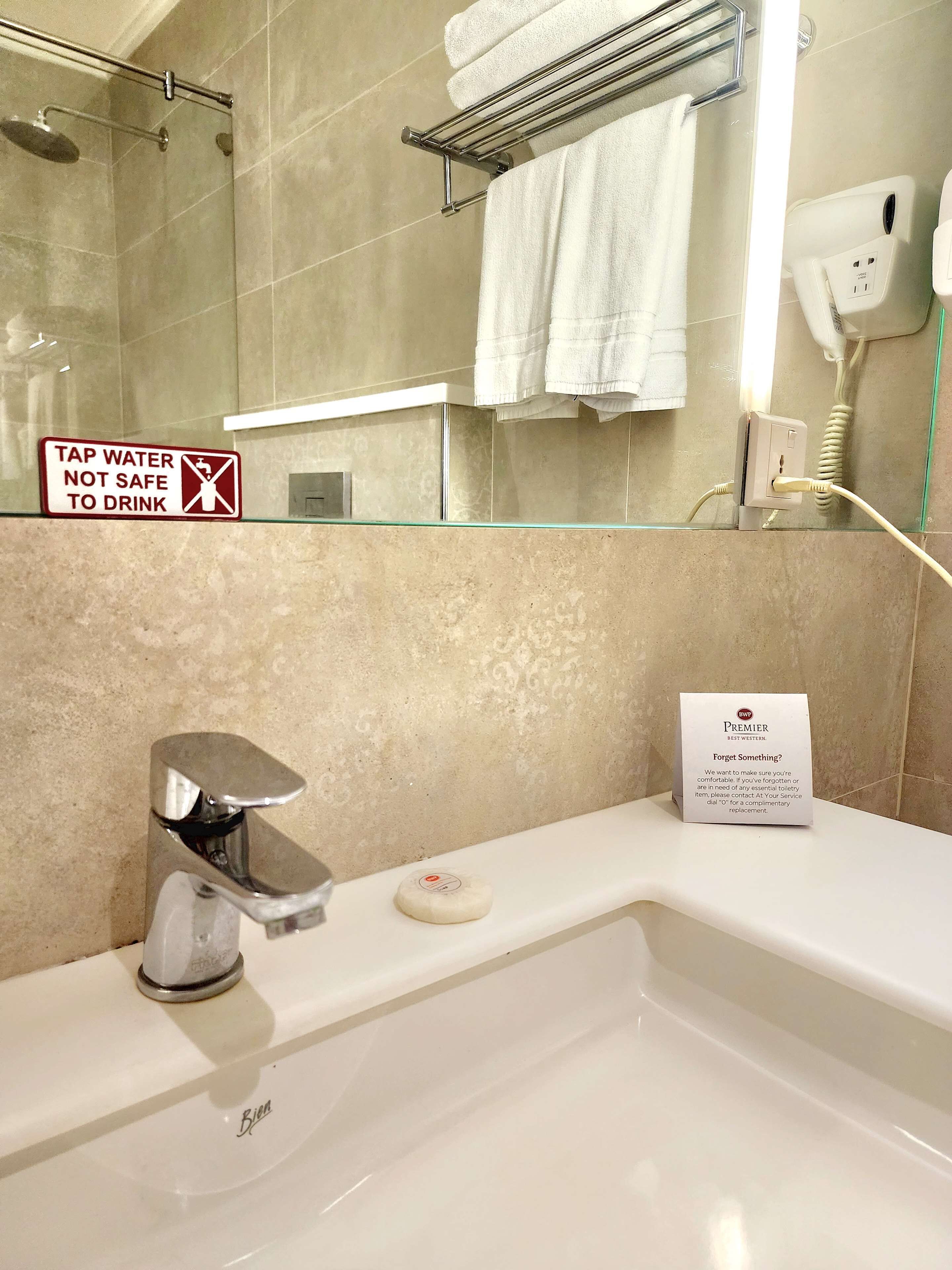 A bathroom with a shower, a sink, a towel rack, and a sign indicating tap water is not safe to drink.