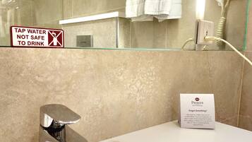 A bathroom with a shower, a sink, a towel rack, and a sign indicating tap water is not safe to drink.