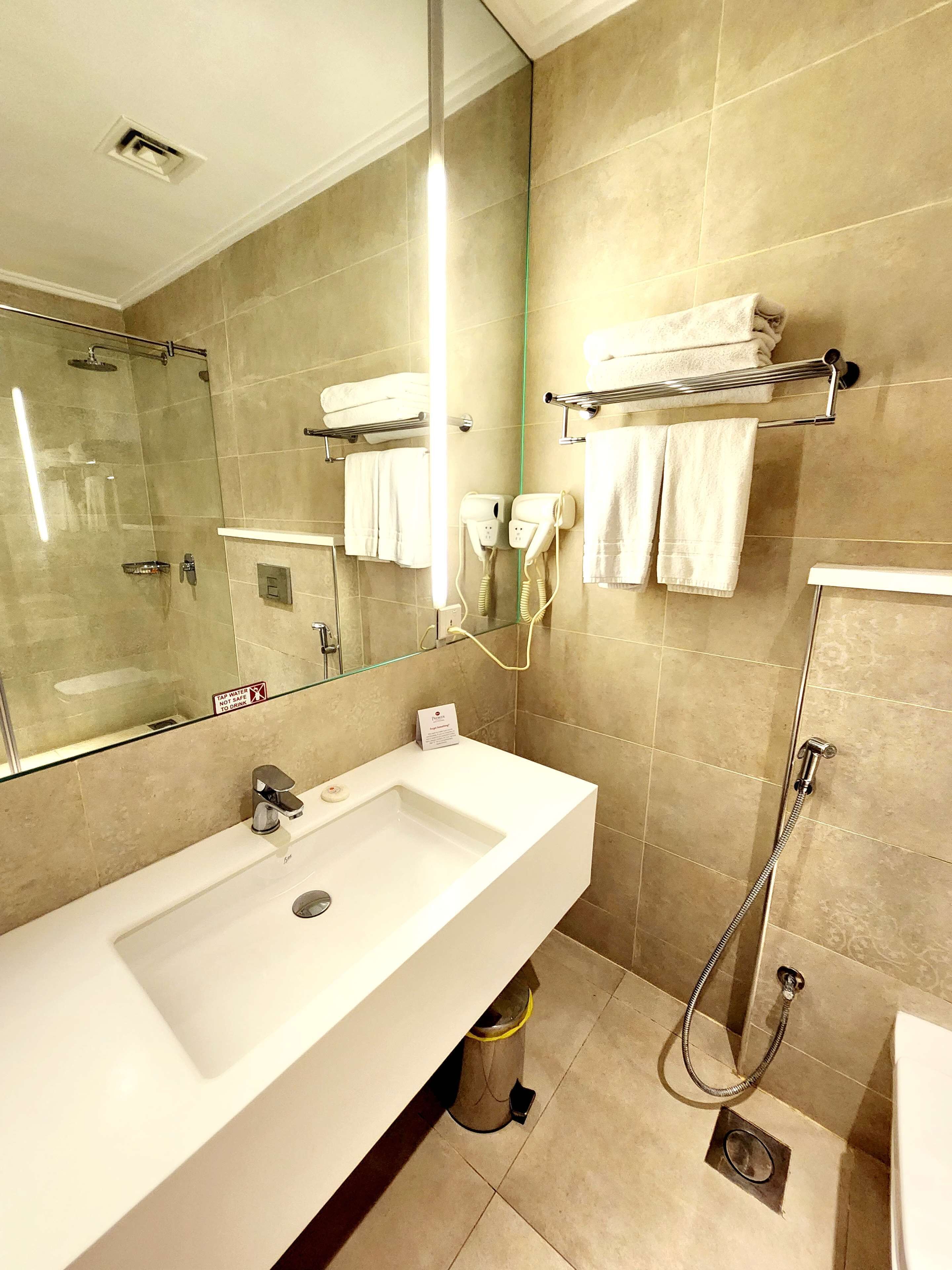 A modern bathroom with a large sink, a mirror, a towel rack, a shower, and a trash can.