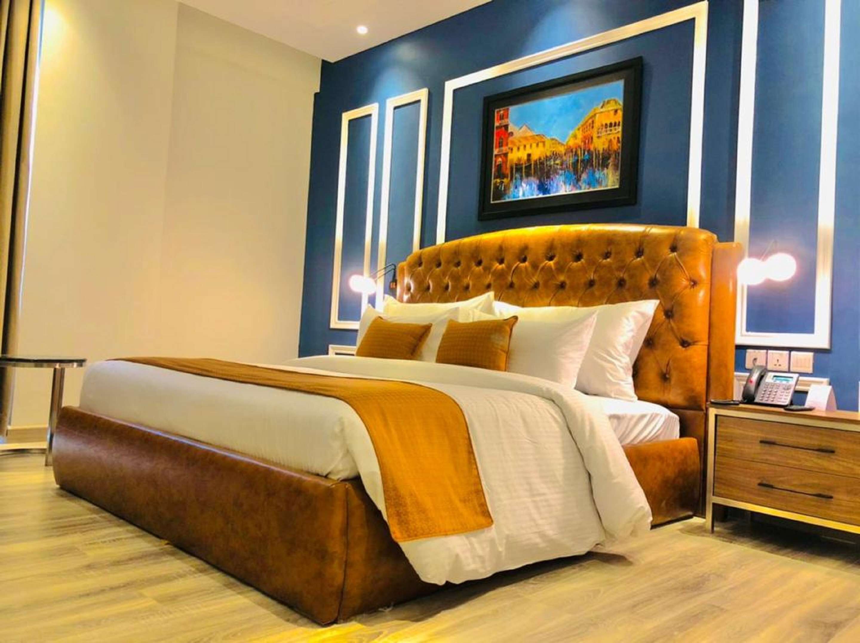 A modern hotel room with a large bed, a wooden nightstand, and a framed painting on the wall.