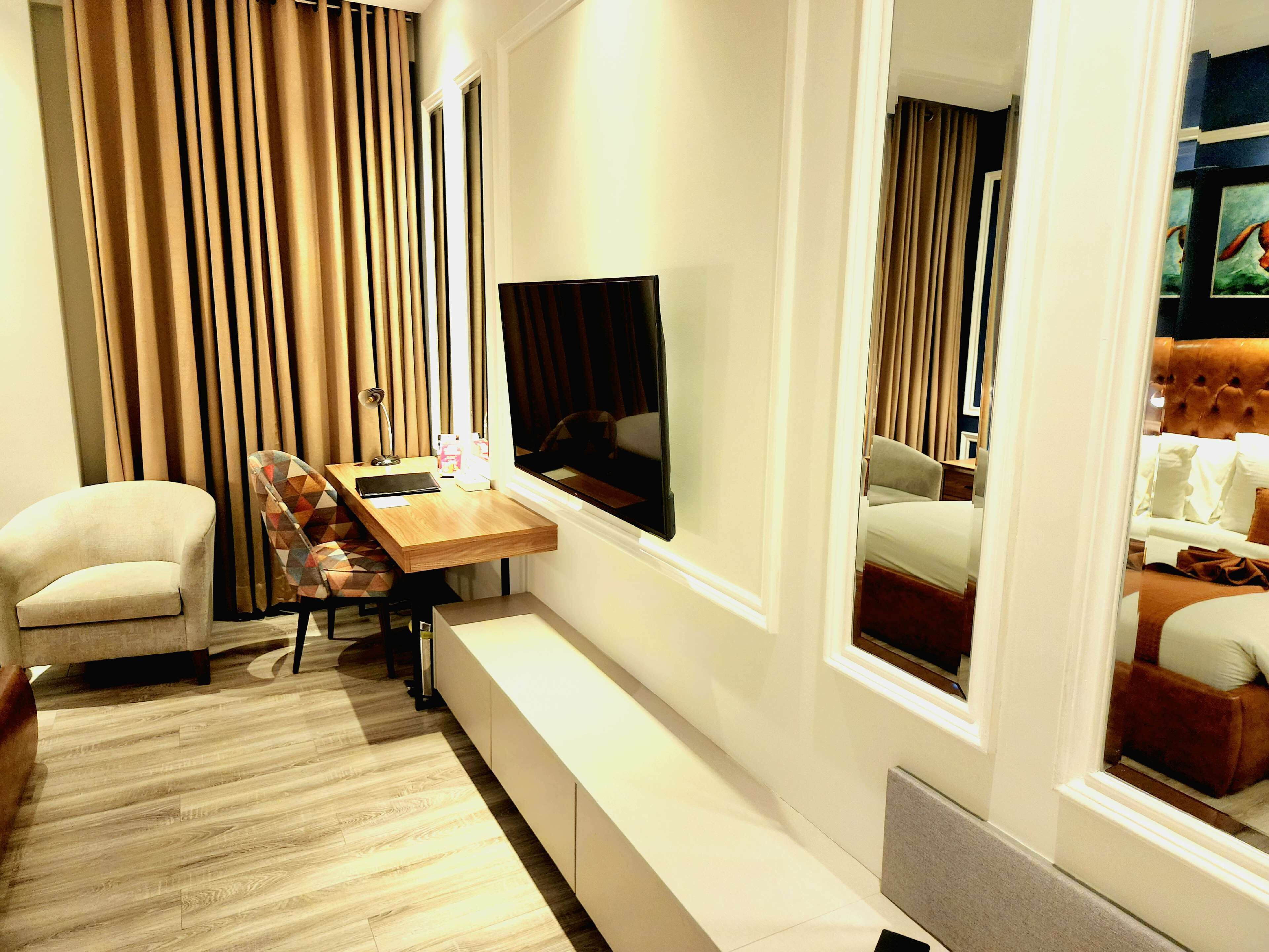 Ein modernes Hotelzimmer mit einem Holzbüro, einem bequemen Sessel, einem großen Flachbildfernseher und einem Bett mit einer gepolsterten Kopfteil.