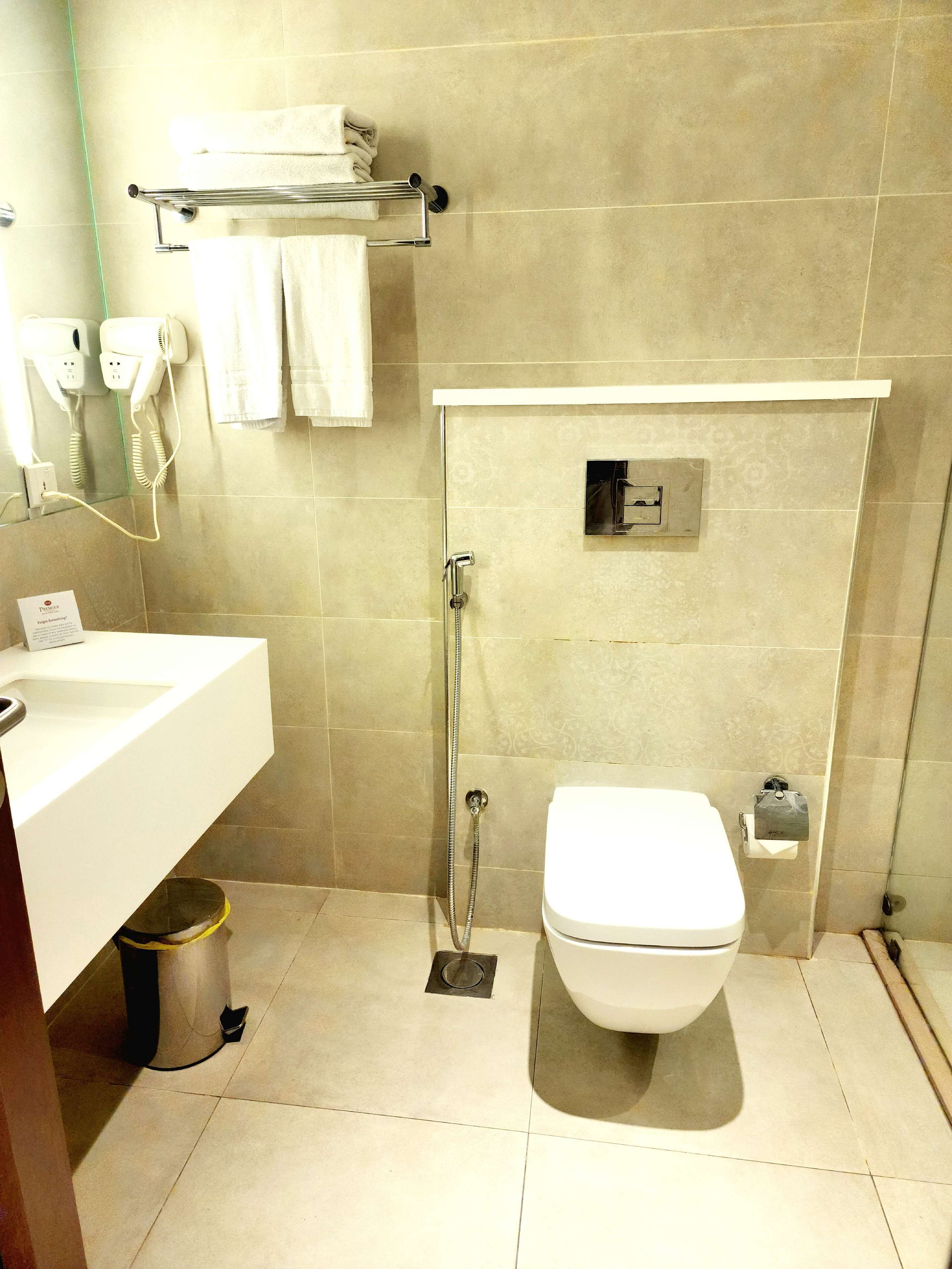 A modern bathroom with a white sink, toilet, and shower. There is a towel rack above the sink and a hairdryer on the wall.