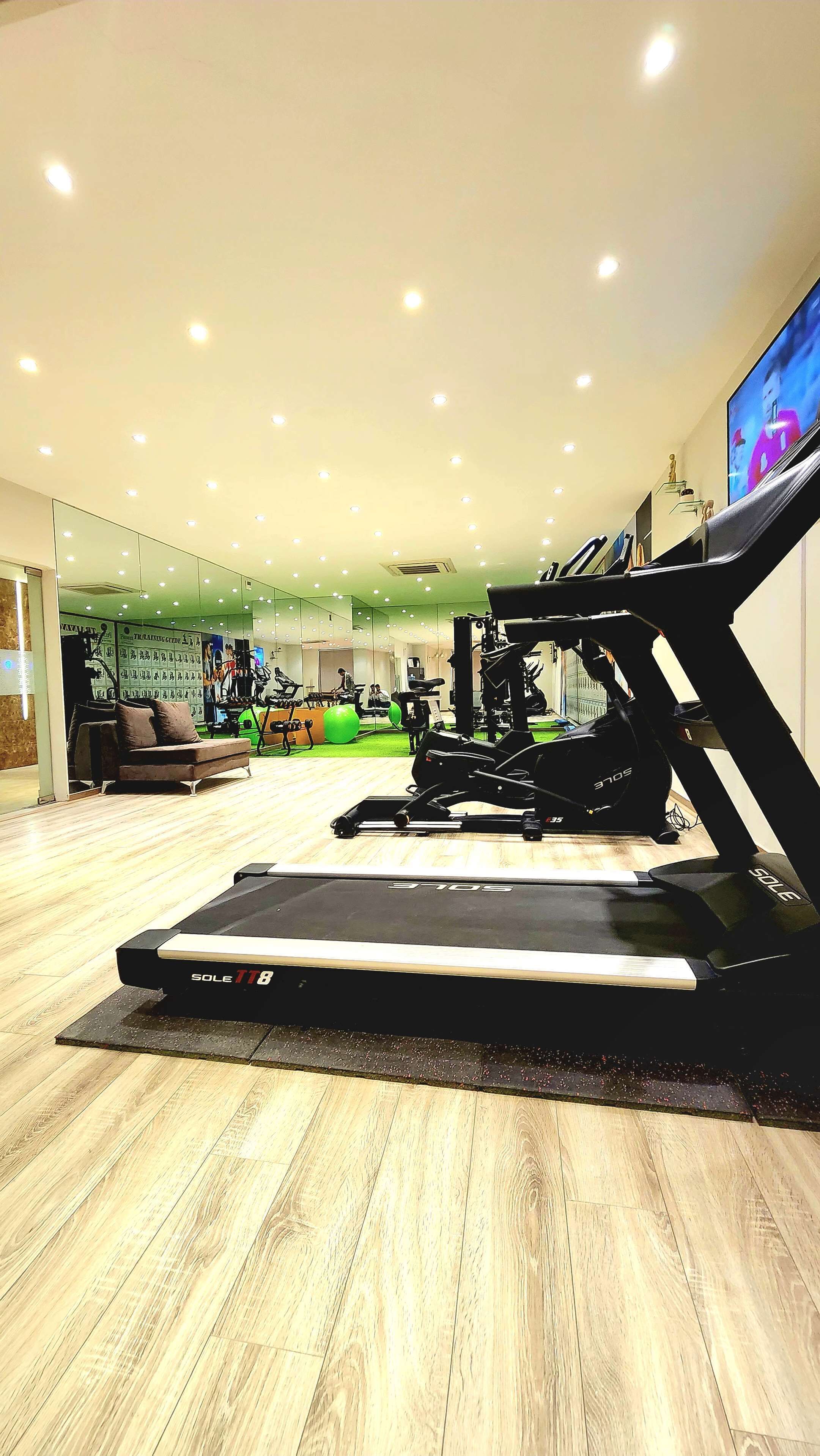 Uma academia com esteiras, bolas de exercício e um espelho grande na parede.