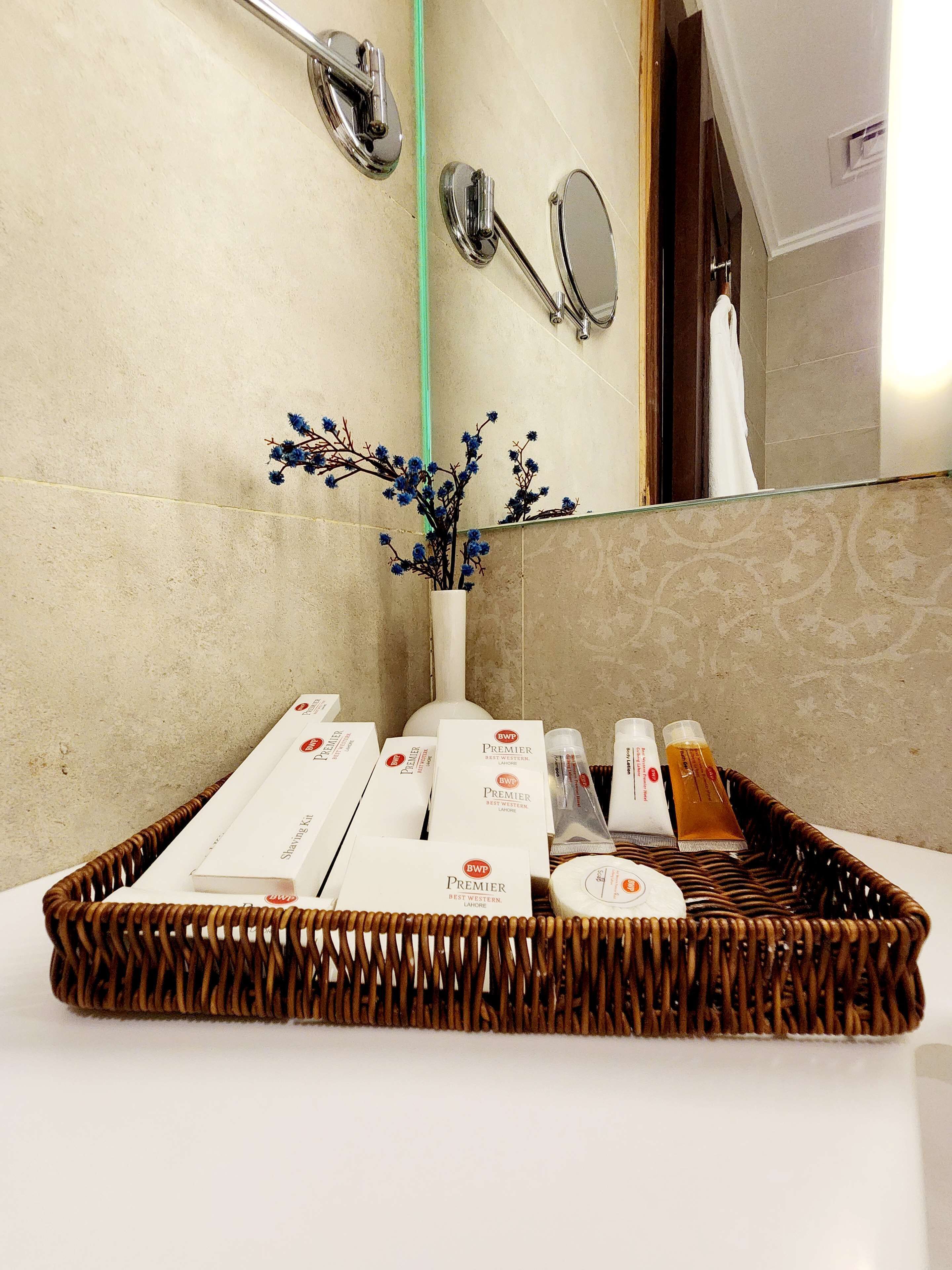 A bathroom with a mirror, a vase with blue flowers, and a tray with toiletries.