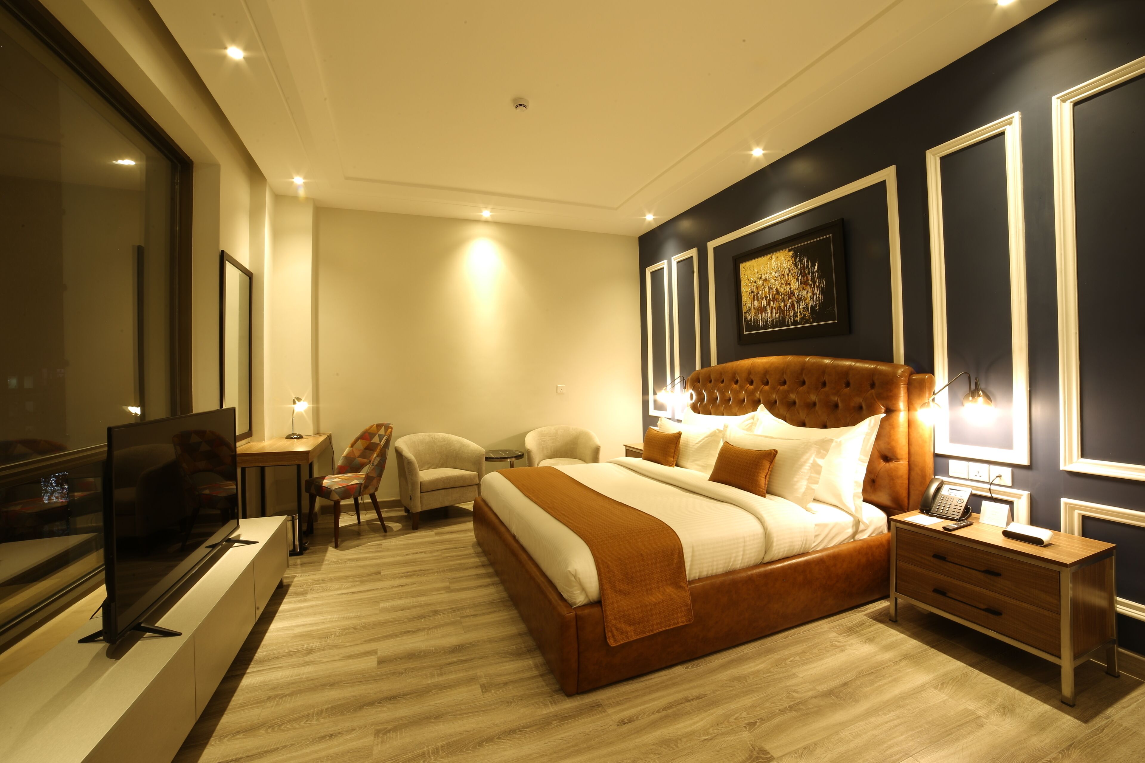 A modern hotel room with a large bed, a TV, a desk, and a chair.