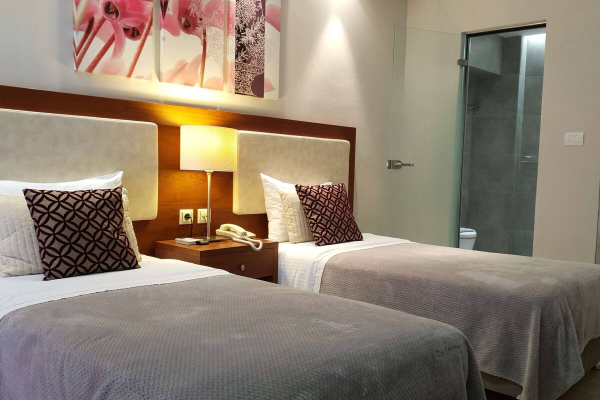 A hotel room with two beds, a bedside lamp, a phone, and a painting on the wall.