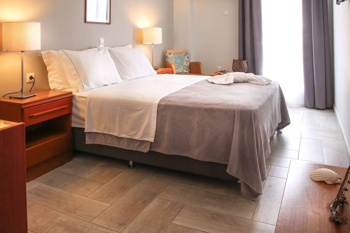 A neatly made bed with white and beige linens, a bedside table with a lamp, and a small nightstand with a lamp.