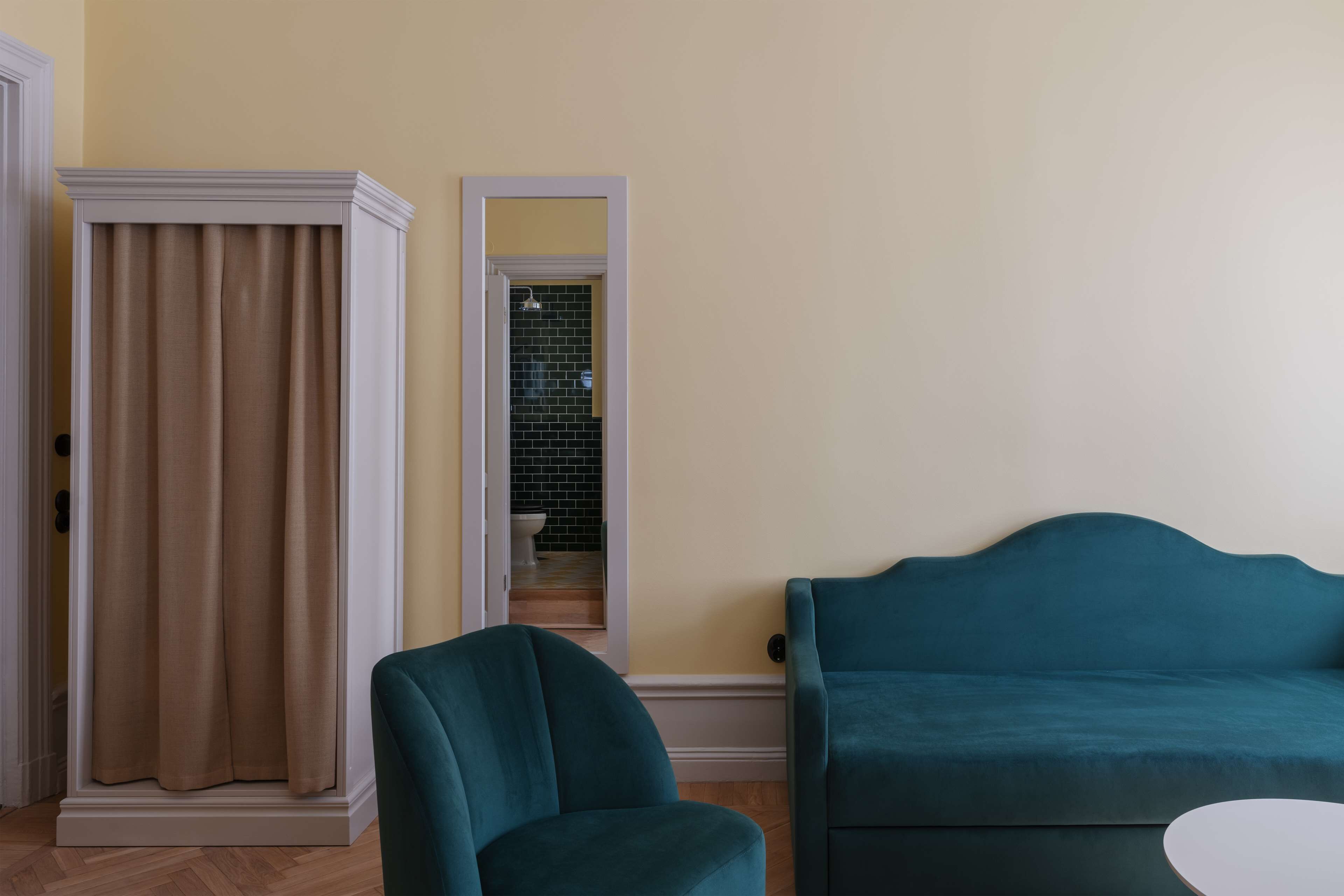 Una habitación con un sofá azul verdoso, una cortina color crema y vistas a un baño con suelo de baldosas.