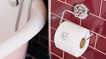 Seinälle kiinnitetty metallinen wc-paperiteline, valkoinen pesuallas ja punaisilla laatoilla päällystetyt seinät.