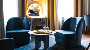 A room with two blue armchairs, a round table with a tray, and a vanity with a mirror and lights. - Hotel Ruth, WorldHotels Crafted  (Stockholm)