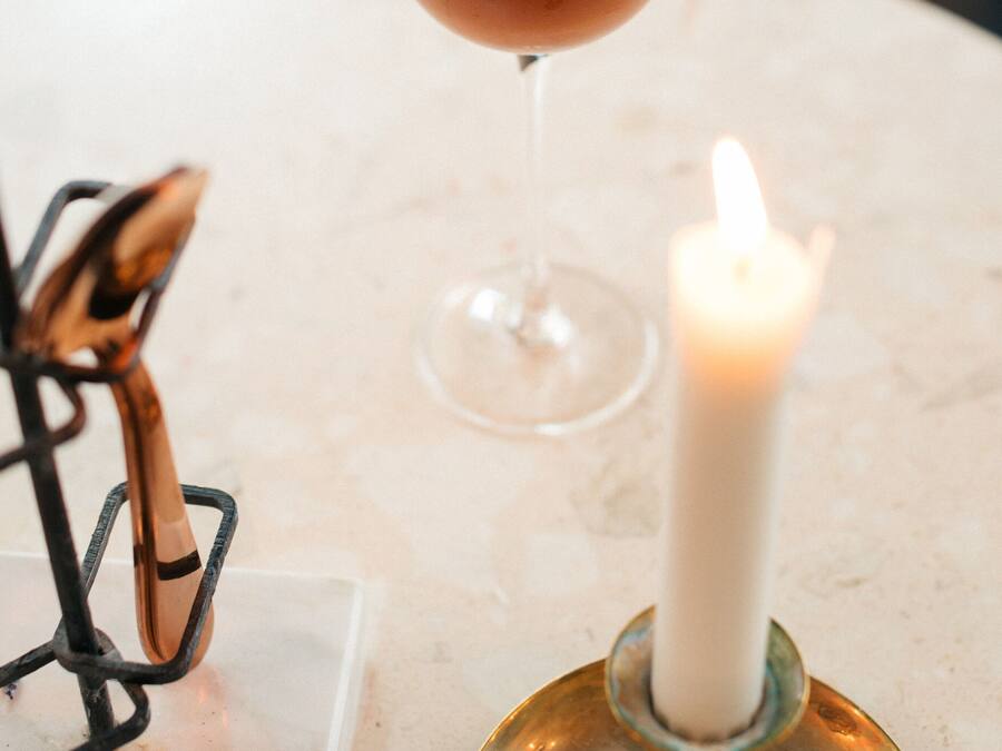 Un cóctel en un vaso sobre una mesa de mármol, con una vela y un portaobjetos para cuchillos al fondo.