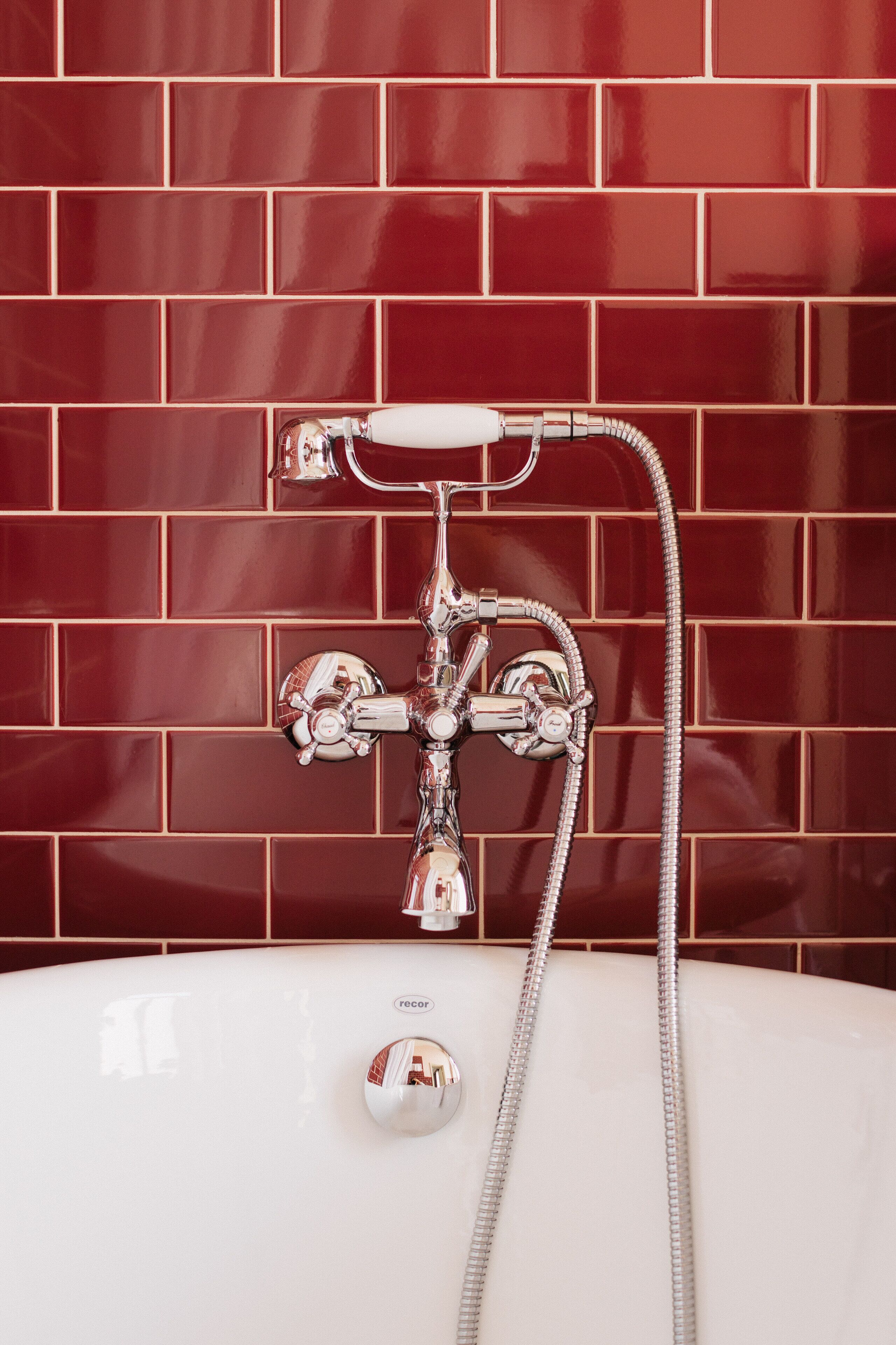 A bathroom with a white bathtub, chrome fixtures, and a red-tiled wall.