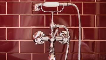 A bathroom with a white bathtub, chrome fixtures, and a red-tiled wall.