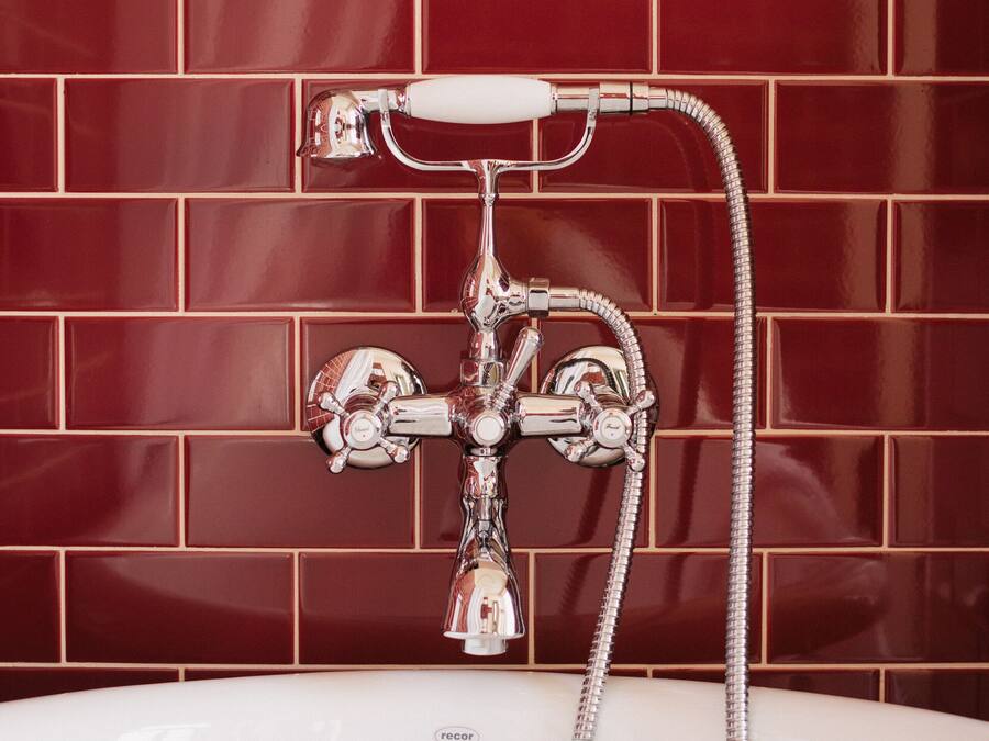 A bathroom with a white bathtub, chrome fixtures, and a red-tiled wall.