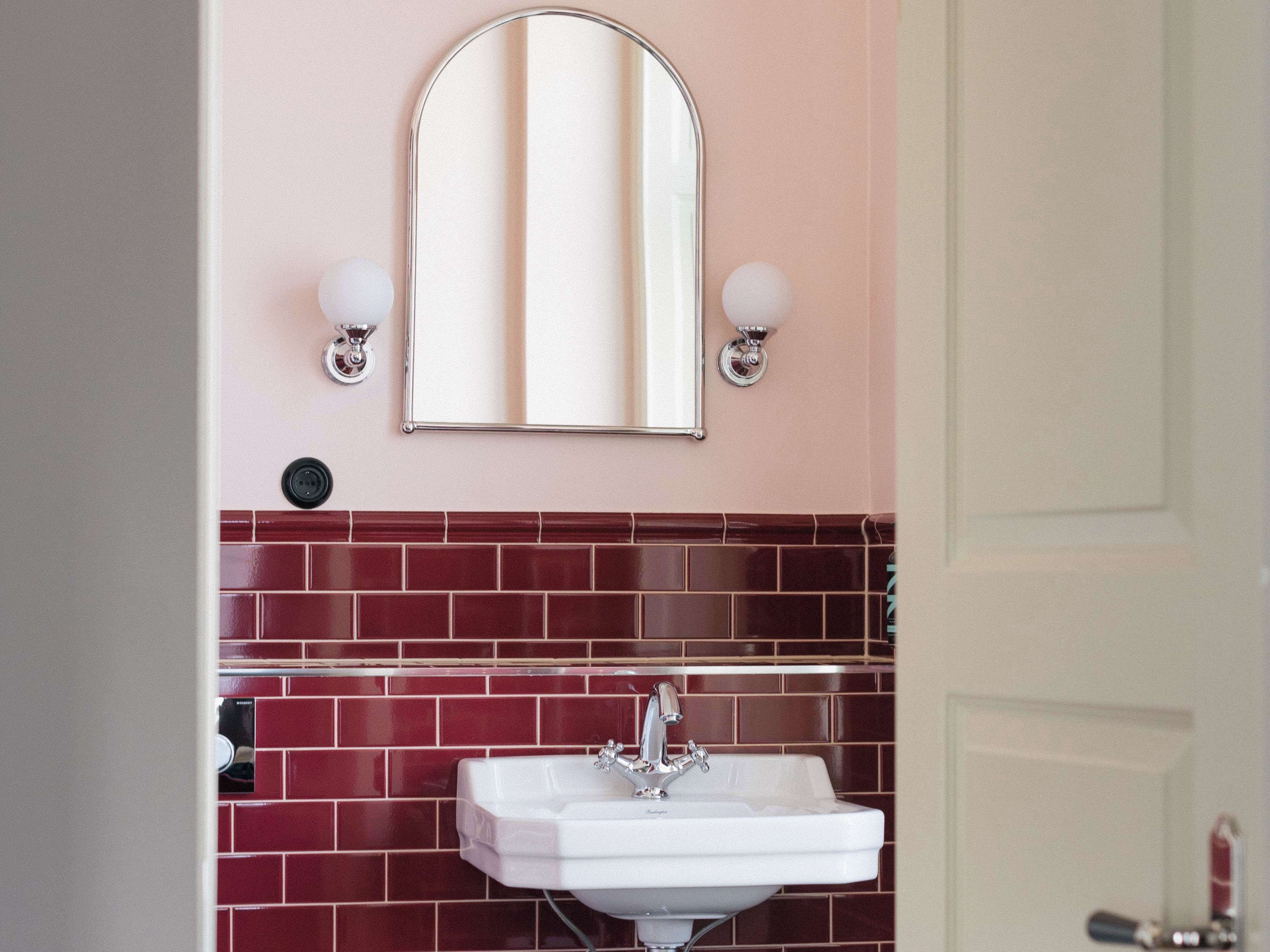 A bathroom with a white sink, red tiled backsplash, and a mirror with wall sconces.
