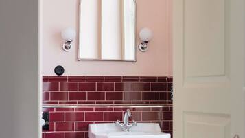 A bathroom with a white sink, red tiled backsplash, and a mirror with wall sconces.