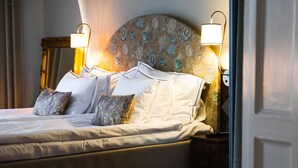 A neatly made bed with white linens and decorative pillows, a floral-patterned headboard, and wall-mounted reading lamps. - Hotel Ruth, WorldHotels Crafted  (Stockholm)