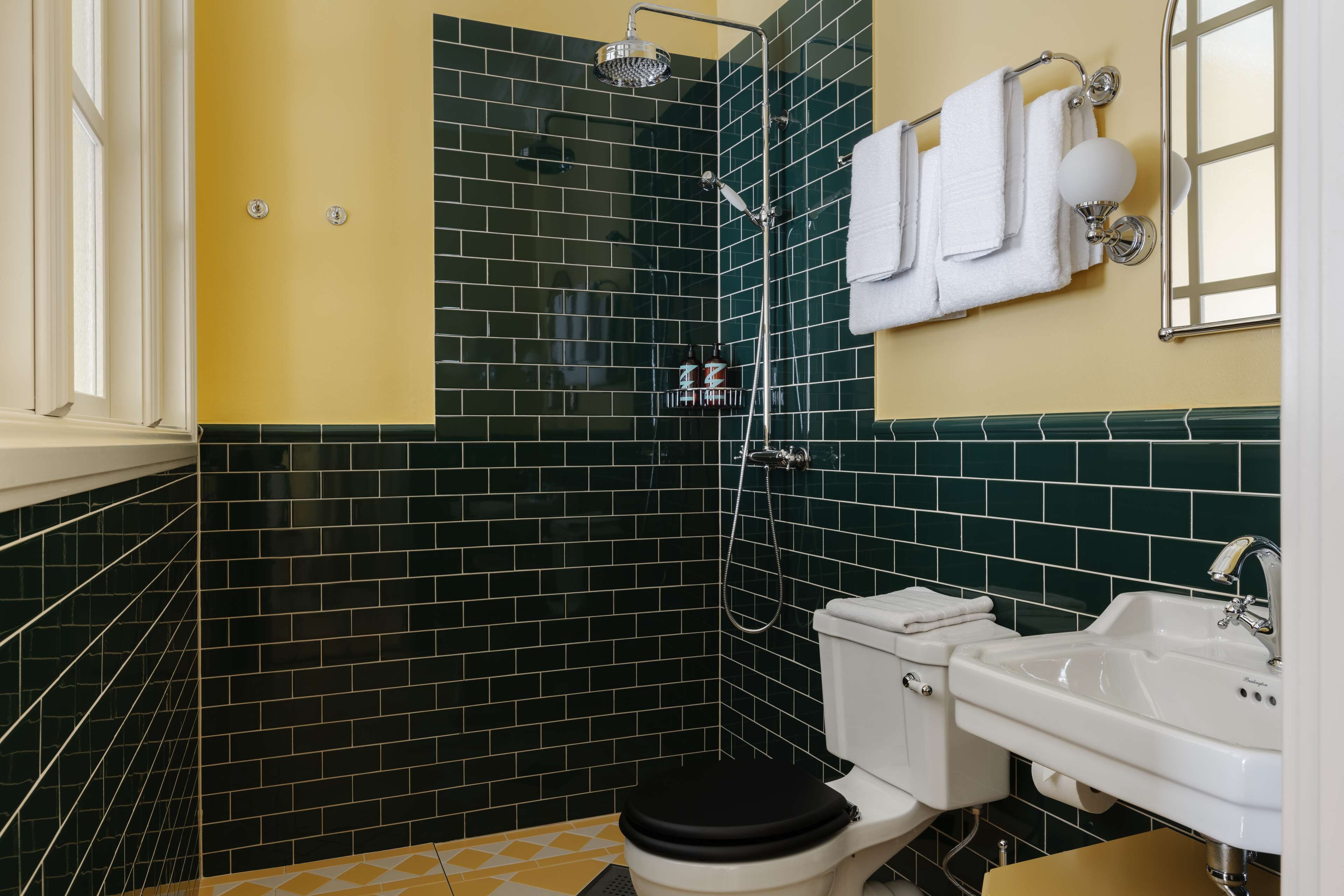A bathroom with a black and yellow tiled wall, a white sink, and a black toilet.