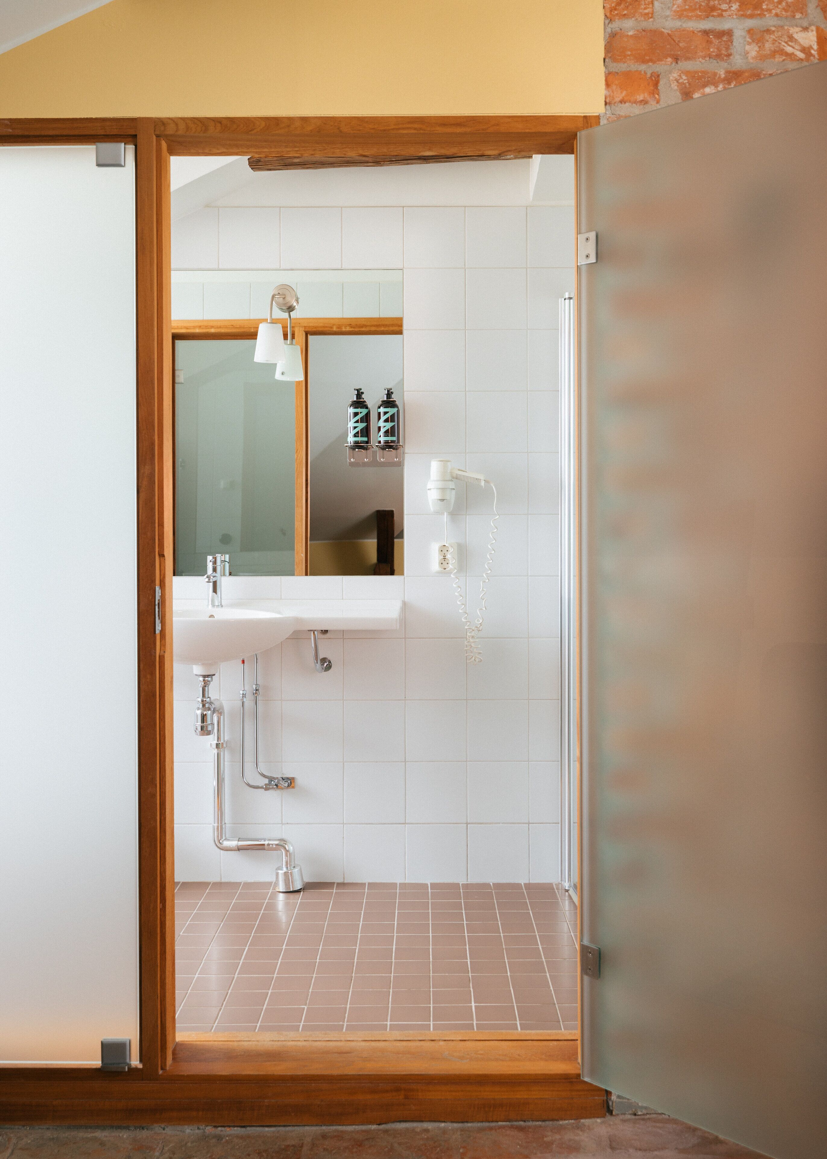 Un baño con puerta de madera, un lavabo blanco, un espejo y zona de ducha.