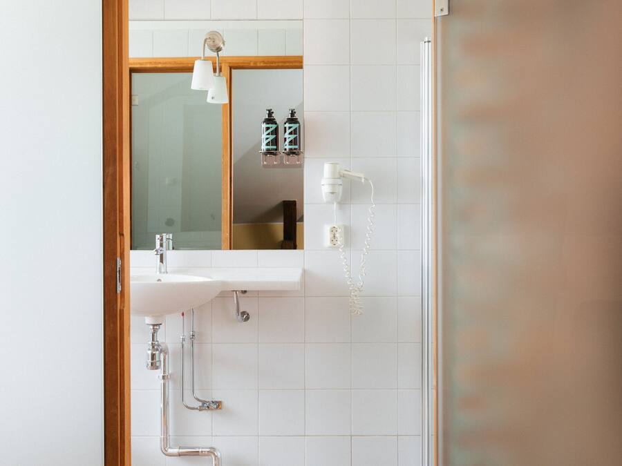 Un baño con puerta de madera, un lavabo blanco, un espejo y zona de ducha.