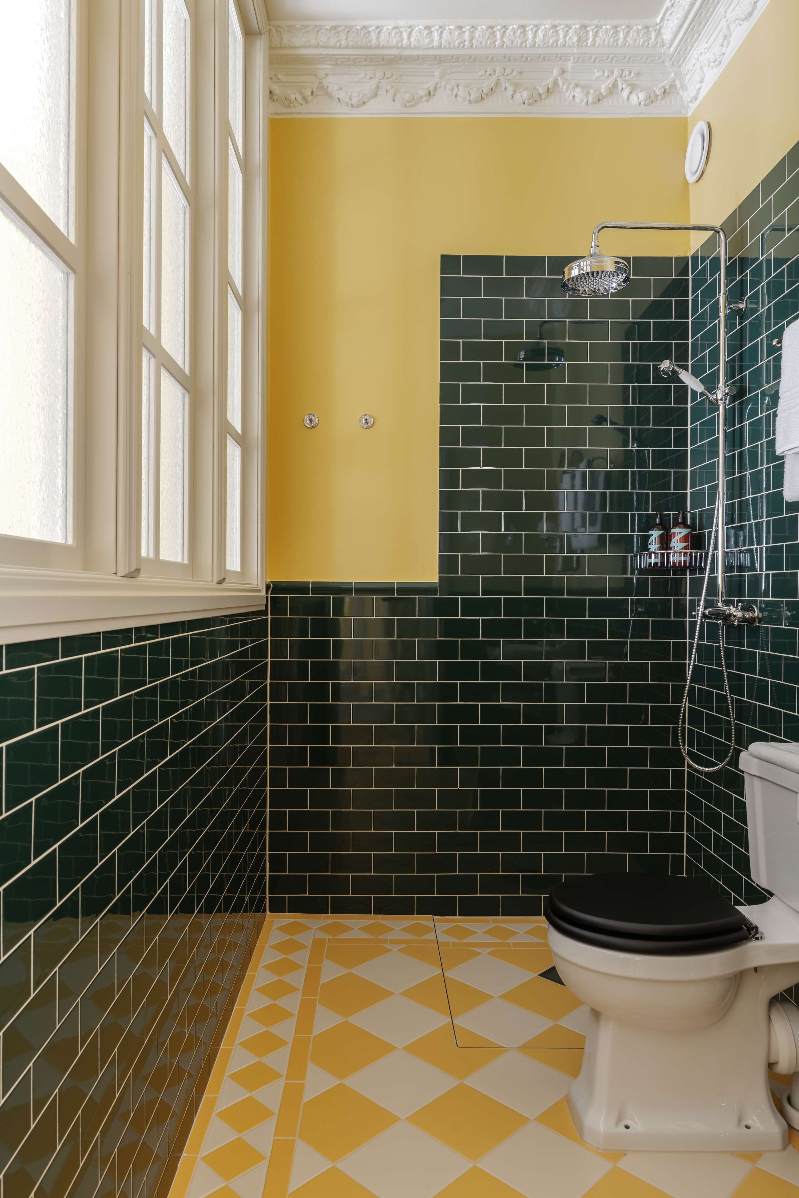 A bathroom with a yellow floor, a black and white toilet, and a shower area with a green tiled wall.