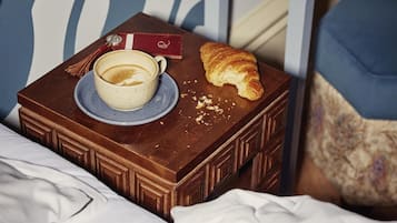 Una cama con un aparador marrón que contiene una taza de café, un croissant y una tarjeta roja.