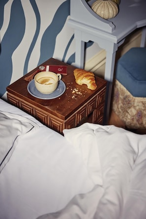 Una cama con un aparador marrón que contiene una taza de café, un croissant y una tarjeta roja.