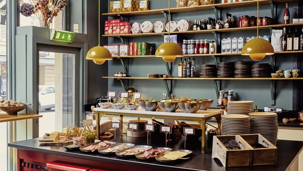 A kitchen area with a central island, red drawers, and hanging pendant lights. Shelves above contain various kitchen items and spices. - Hotel Ruth, WorldHotels Crafted  (Stockholm)