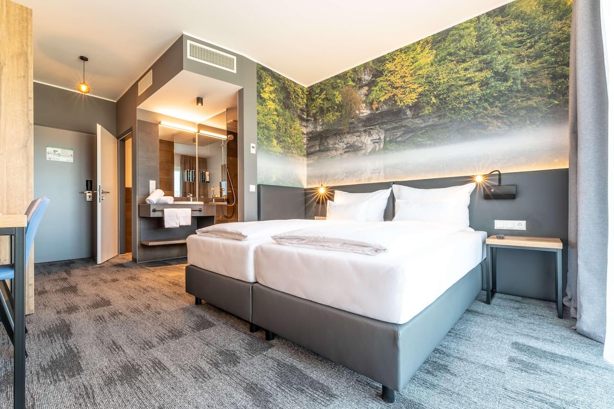 Ein modernes Hotelzimmer mit einem großen Bett, einem Schreibtisch, einem Spiegel und einem Wandbild.