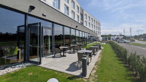 A modern building with a glass facade, outdoor seating area with tables and chairs, and a grassy lawn. - Aiden by Best Western Stadtgut Hotel Steyr (Steyr)