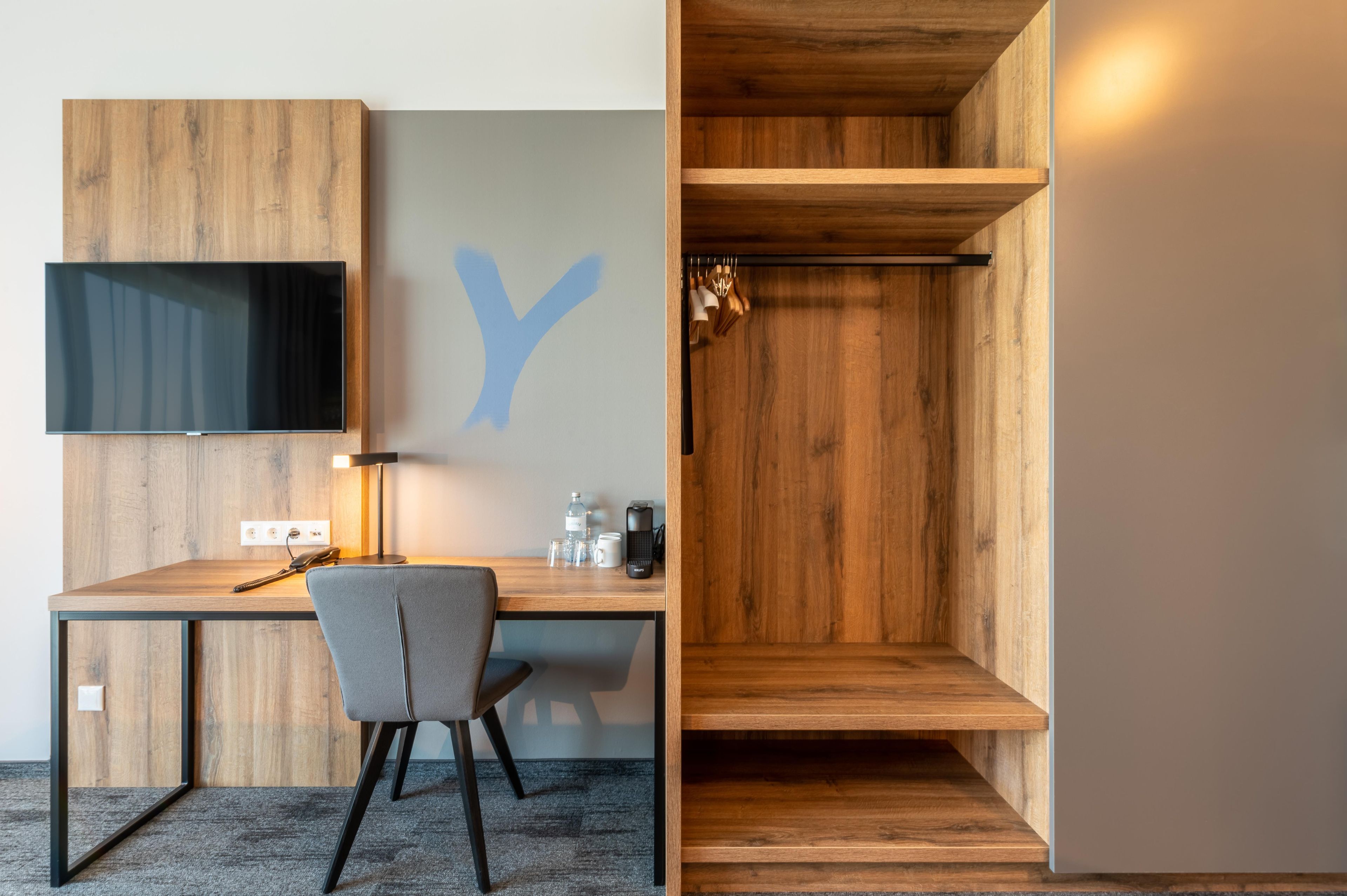 A modern office space with a desk, chair, flat-screen TV, and a wooden wall with a large letter 'Y'.