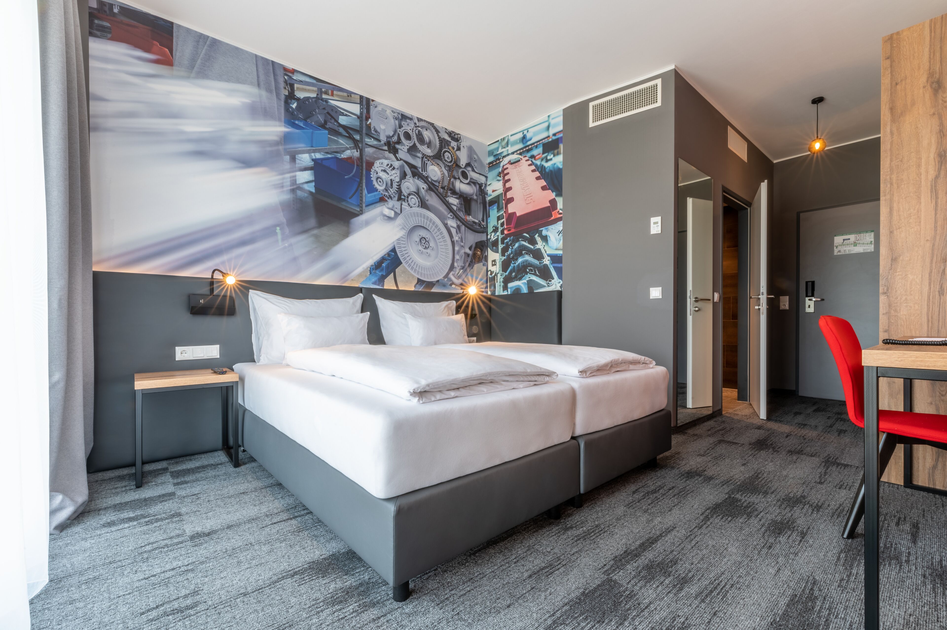 A modern hotel room with a large bed, a desk, and a chair.