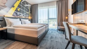 A hotel room with a bed, a desk, a chair, a TV, and a large window with curtains. - Aiden by Best Western Stadtgut Hotel Steyr (Steyr)