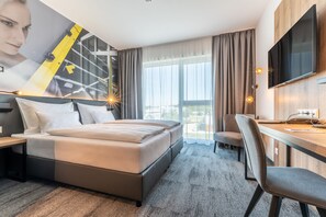 A hotel room with a bed, a desk, a chair, a TV, and a large window with curtains. - Aiden by Best Western Stadtgut Hotel Steyr (Steyr)