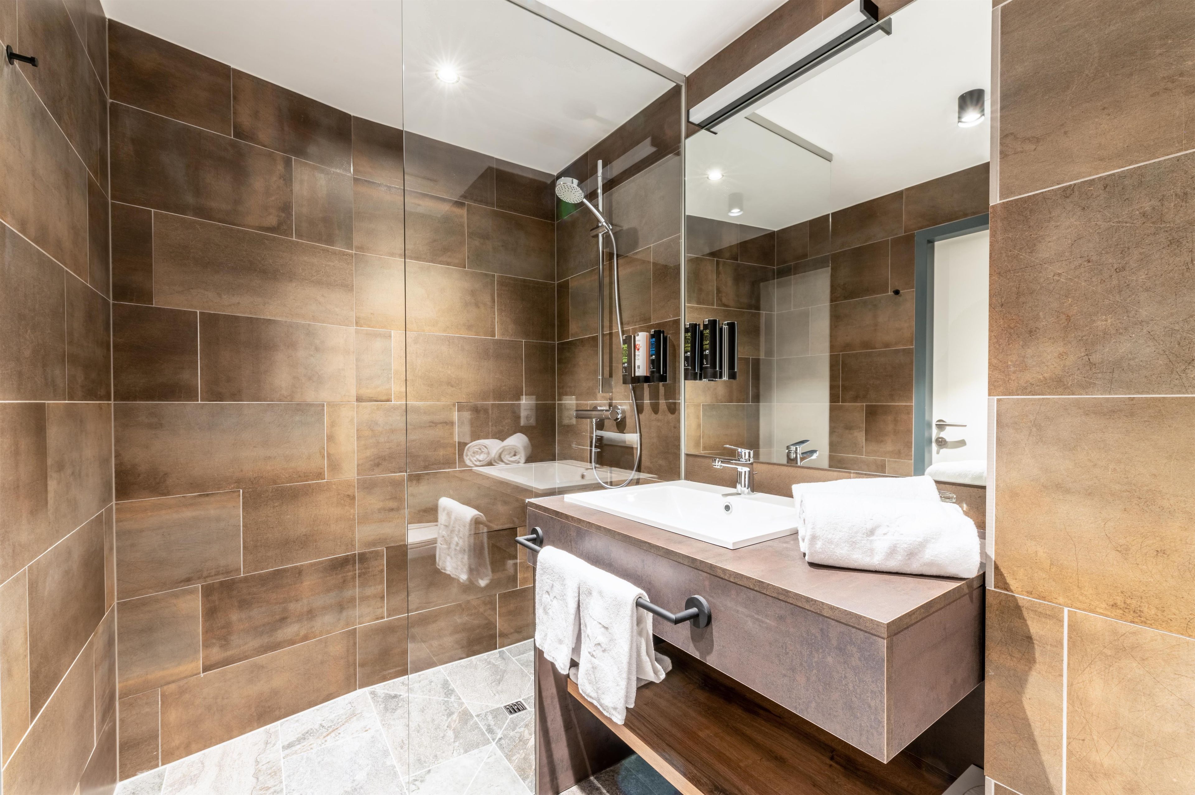 A modern bathroom with a large mirror, a shower, and a vanity with a sink.