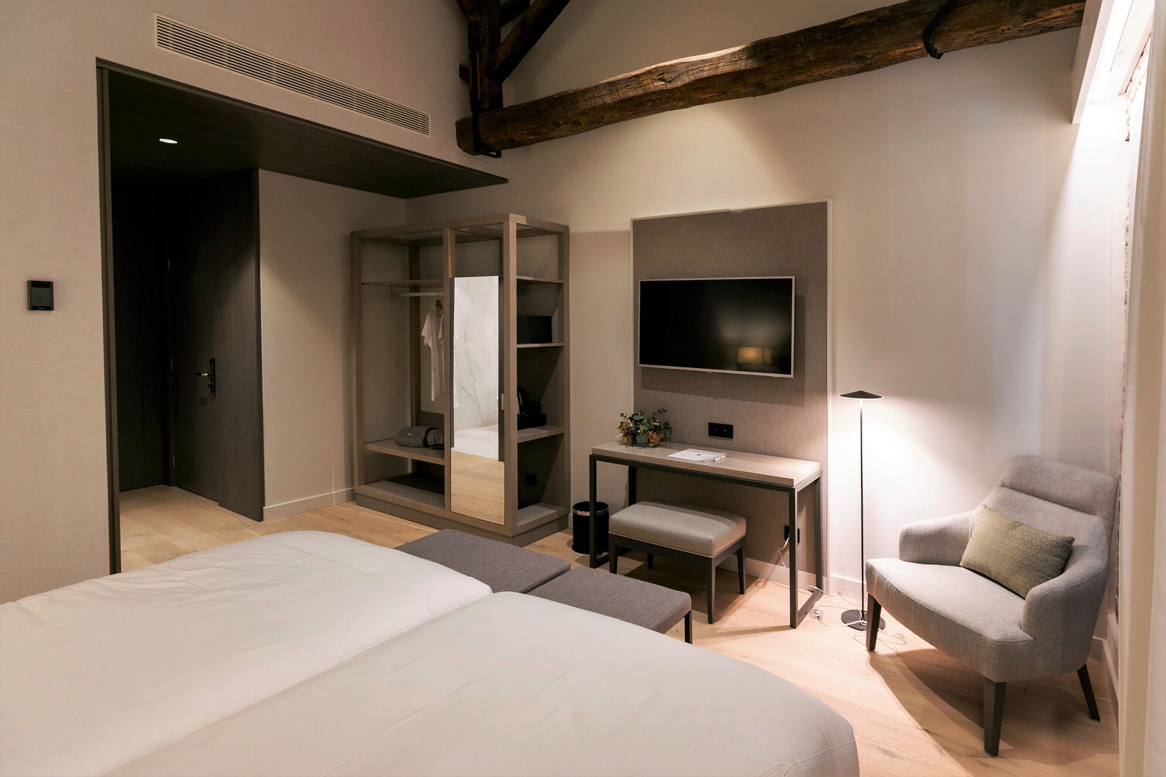 A bedroom with a bed, a desk, a chair, a wardrobe, and a TV.