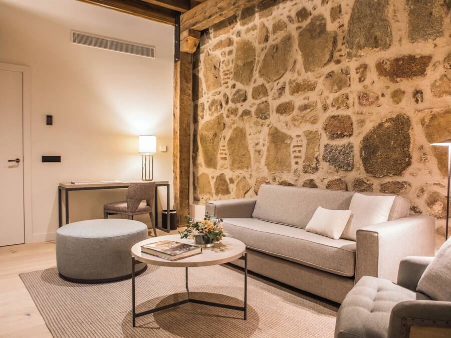 Una sala de estar acogedora con pared de piedra, un sofá, un otoman redondito, una mesa de centro y una lámpara.
