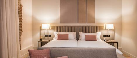 Hotelkamer met een groot bed, twee nachtkastjes met lampen, een grijze bank met kussens en een accentmuur van baksteen.
