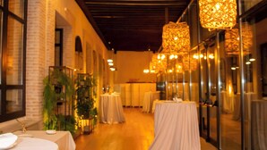 A corridor with tables set up for dining, wooden flooring, and hanging lamps. - Sofraga Palacio (Ávila)