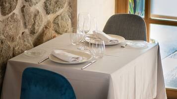 Una mesa de comedor dispuesta con platos, vasos y cubiertos, ubicada frente a una pared de piedra con una ventana al fondo.