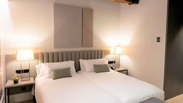 A modern bedroom with a large bed, bedside lamps, a bench, and exposed wooden beams.